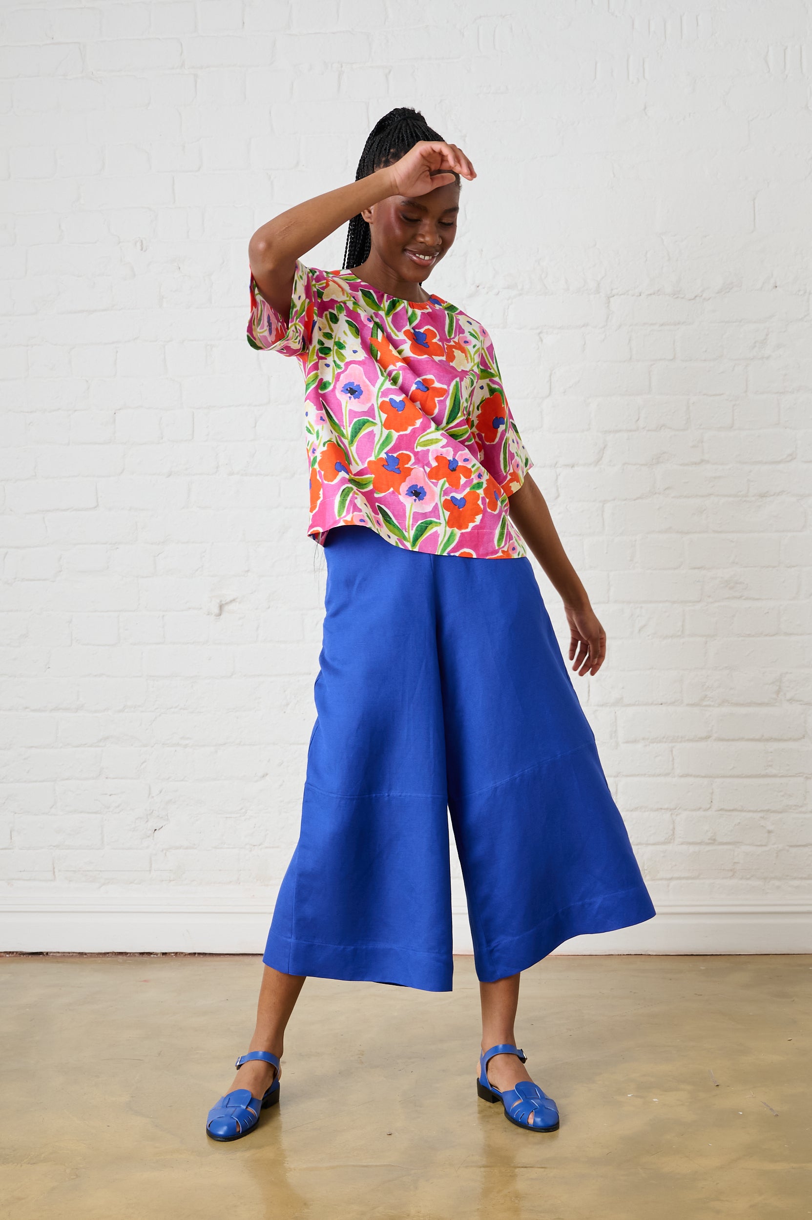 Model is wearing blue linen pants with a floral top and blue sandals