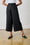 Model is wearing black wide leg linen pants with a white top and black sandals