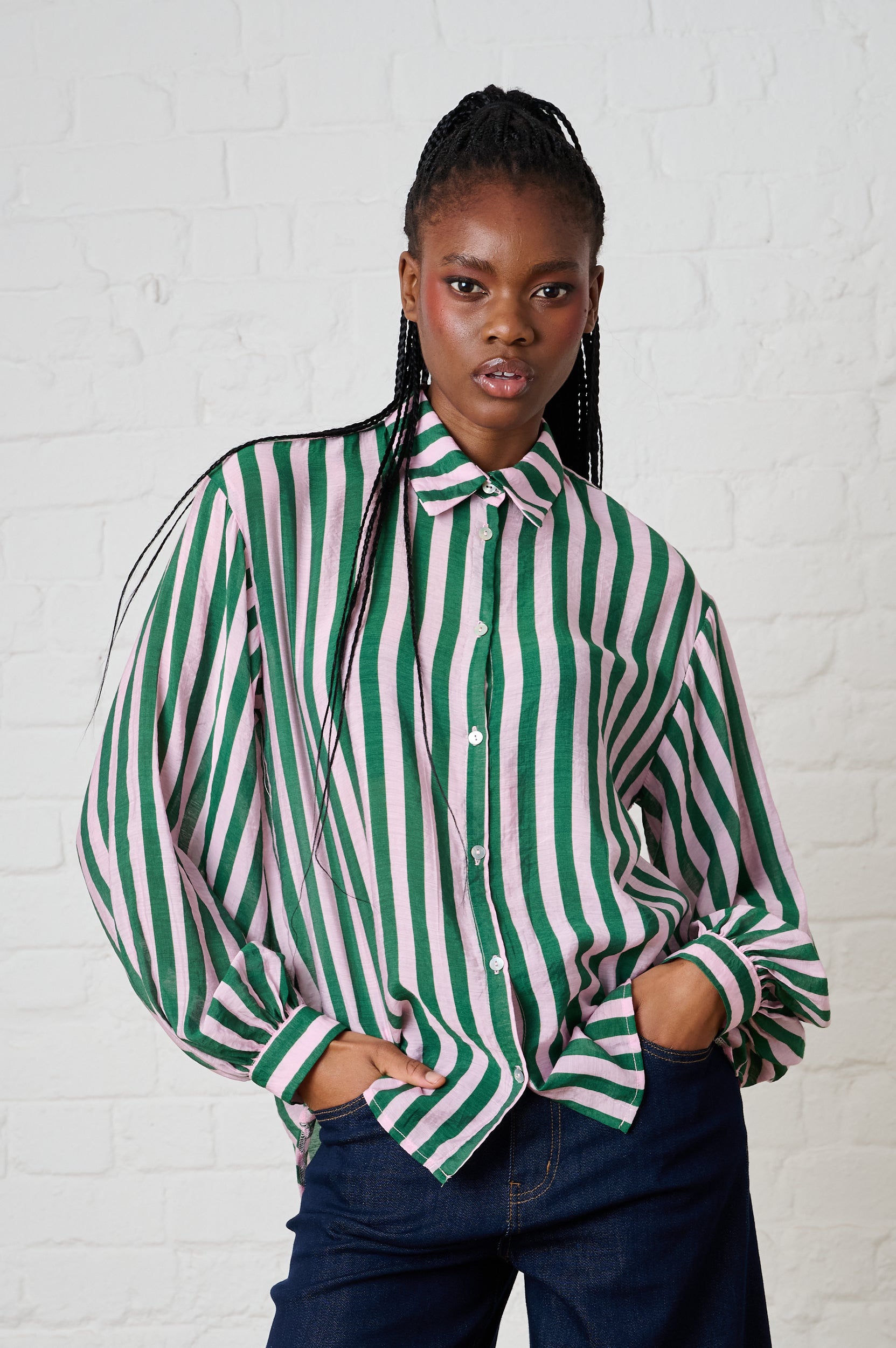 Model is wearing a green and pink stripe bellow sleeve shirt with blue denim jeans