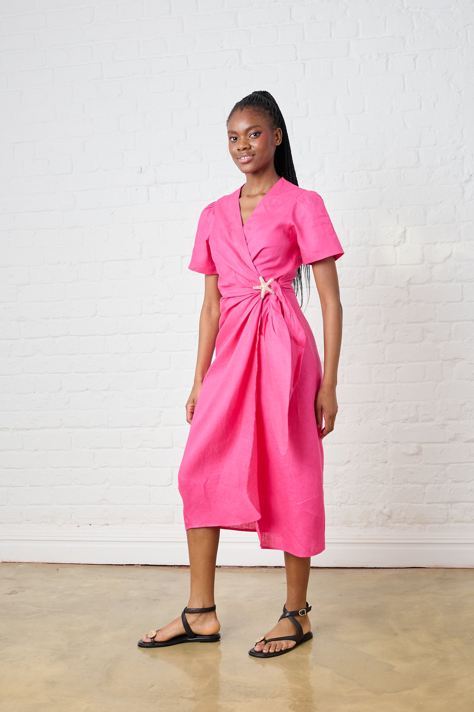 Model is wearing a pink wrap dress with black sandals