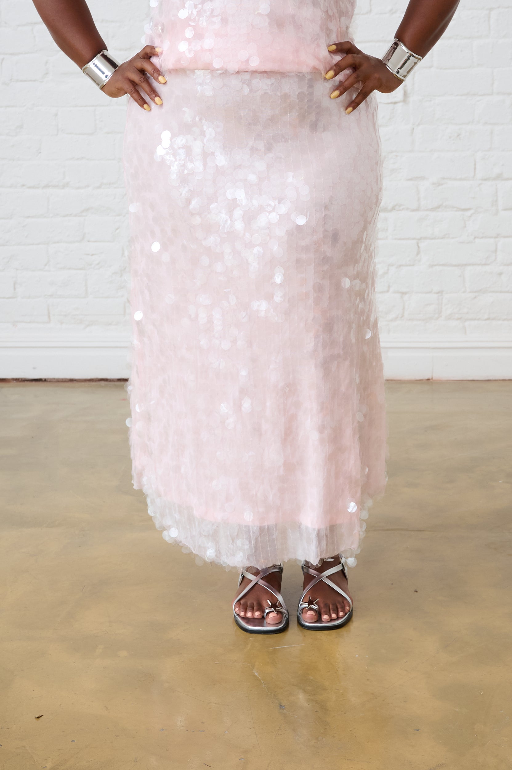 Model is wearing a light pink sequin skirt and silver sandals