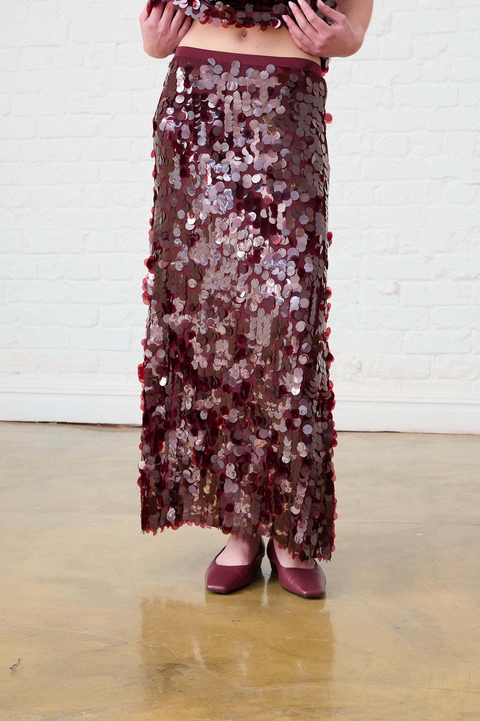 Model is wearing a burgundy sequin maxi skirt with burgundy flats