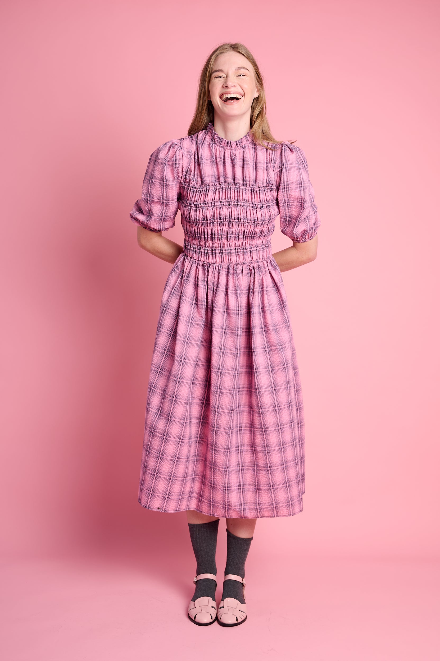 Model is wearing an empire dress in pink check with charcoal socks and pink shoes