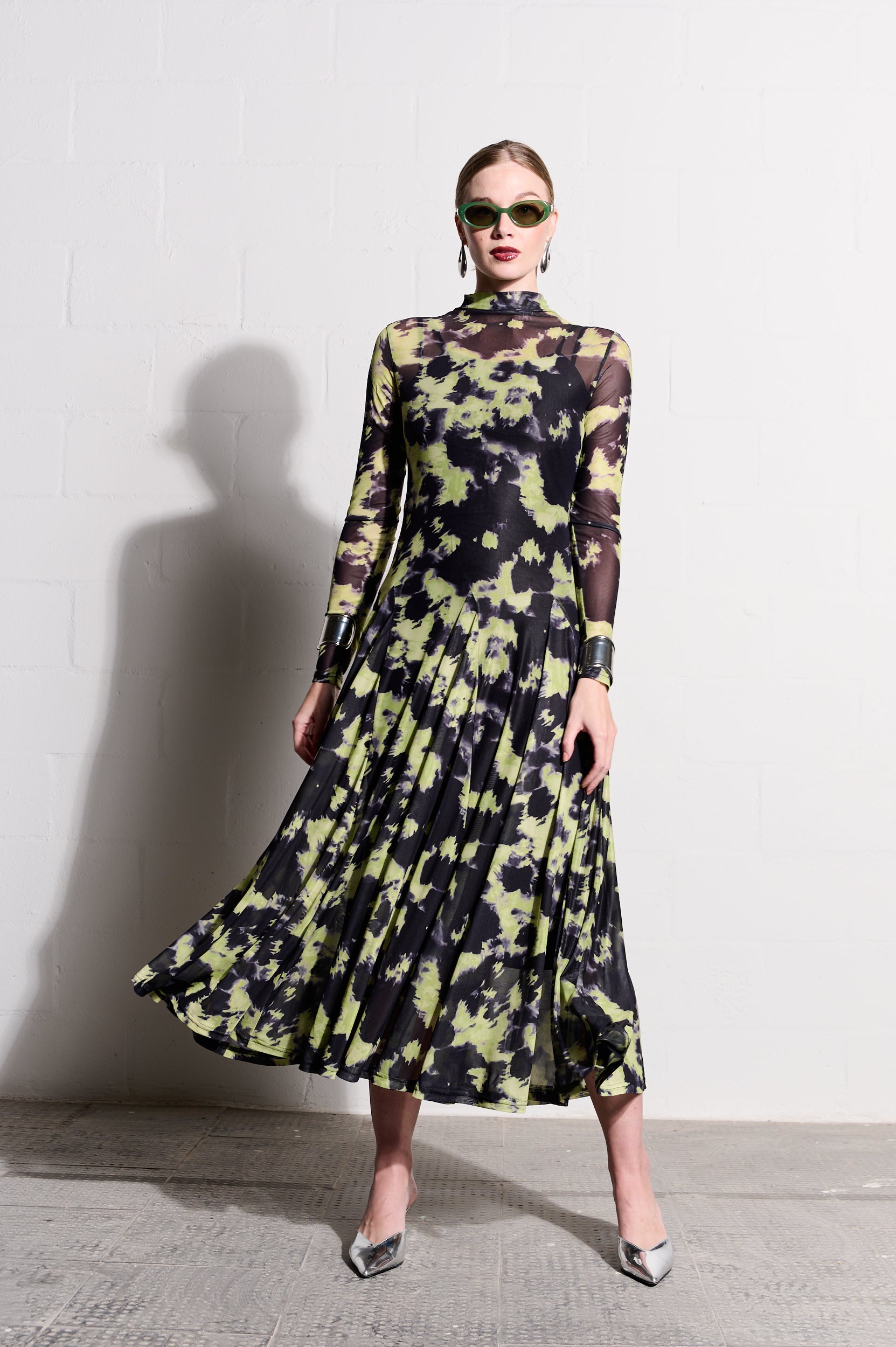 Model is wearing a yellow and black long sleeve mesh dress with silver shoes