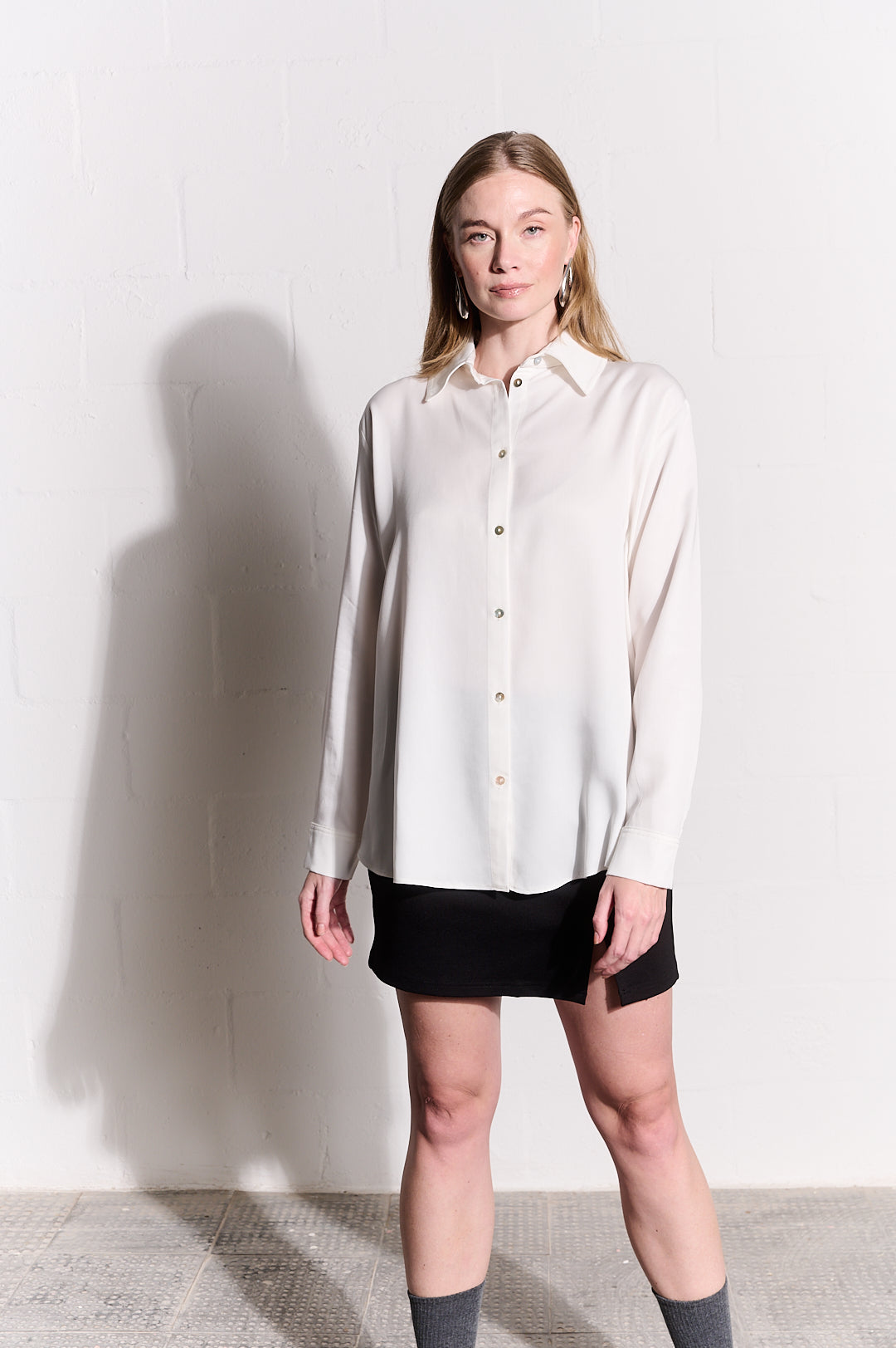 Model is wearing a long sleeve top in milk with a black mini skirt