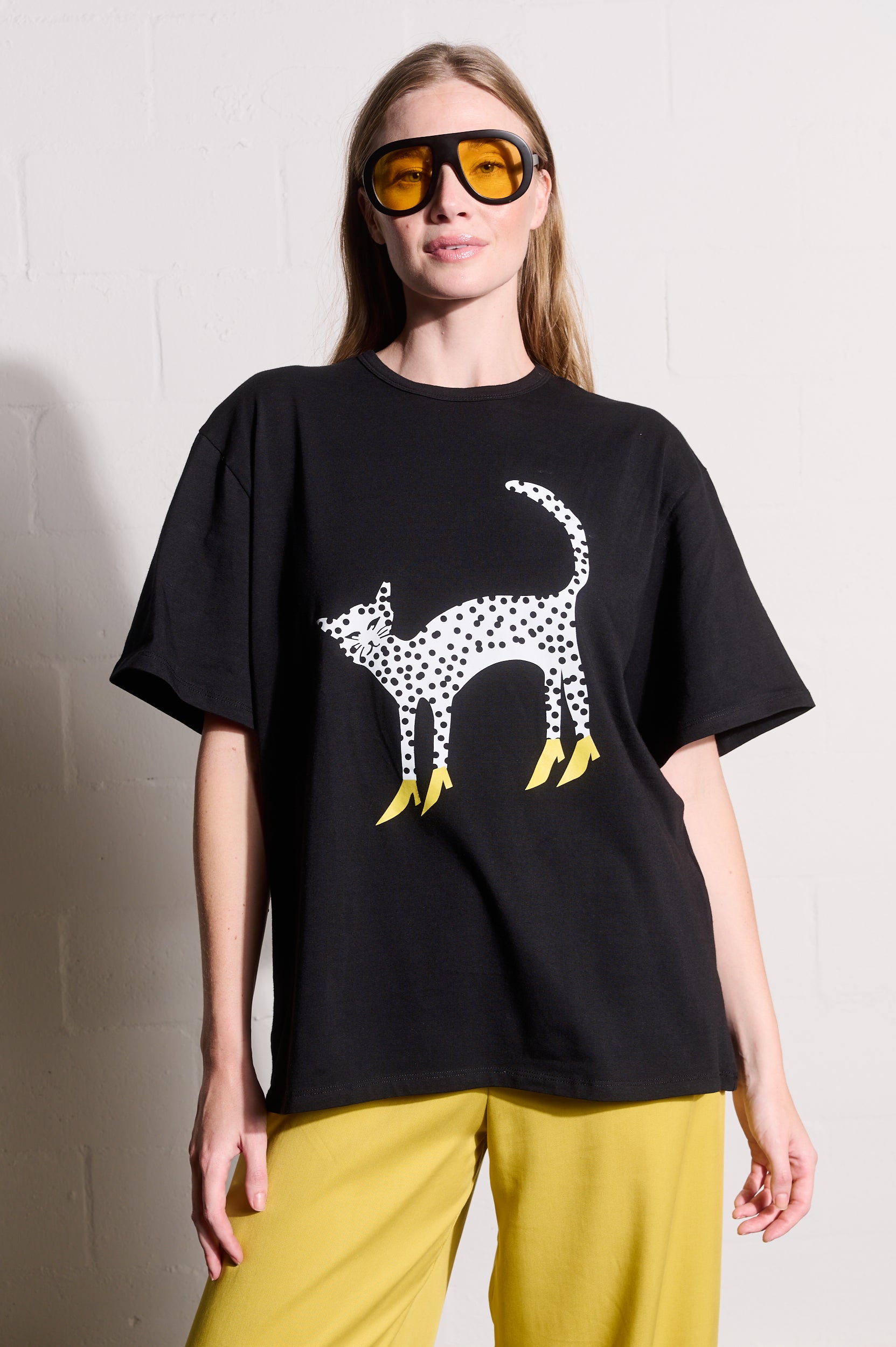 Model is wearing a black top with a cheetah in heels print and yellow pants