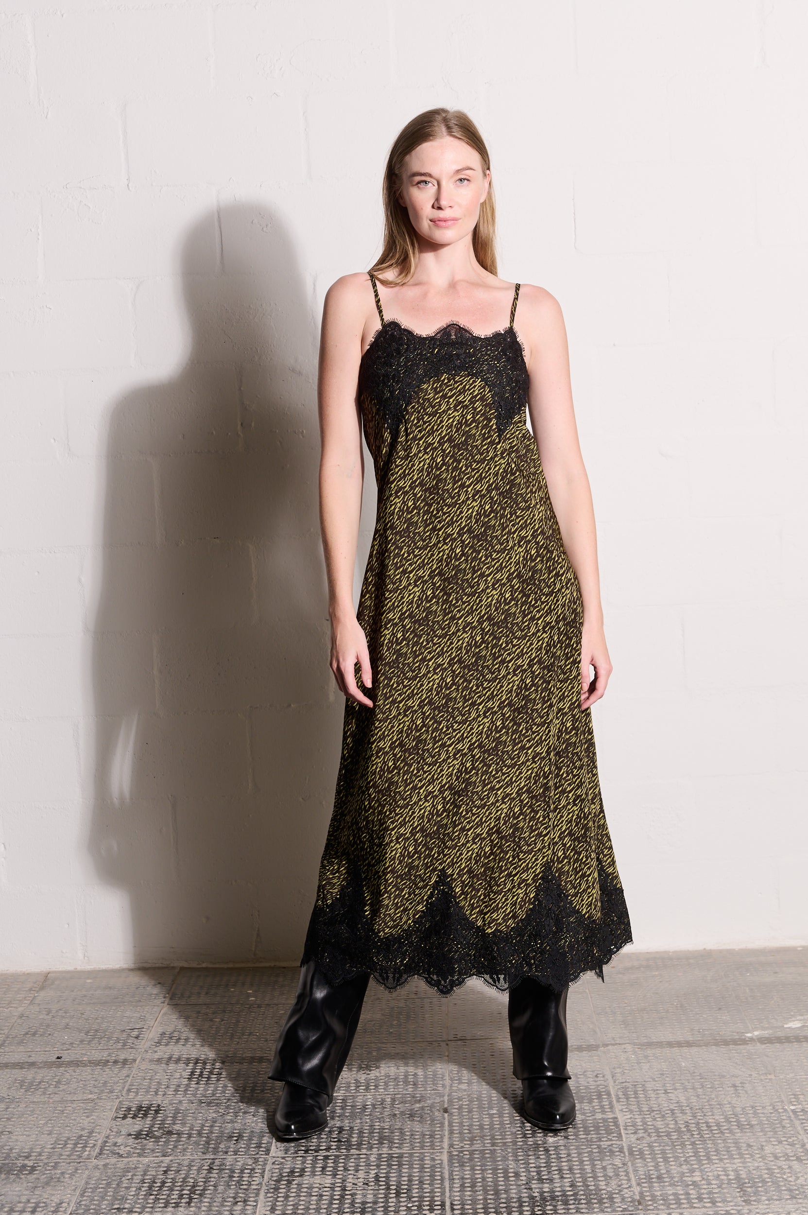 Model is wearing a slip dress in yellow and black with lace detail and black boots