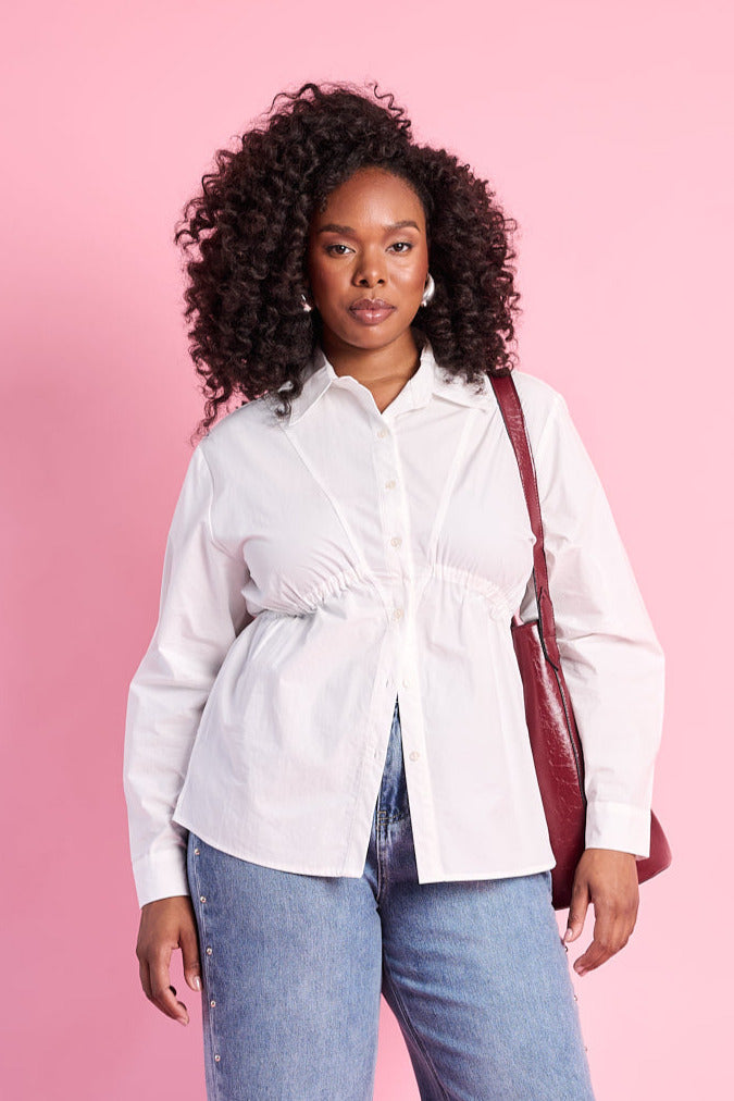 Model is wearing white long sleeve button up with denim jeans and a red bag