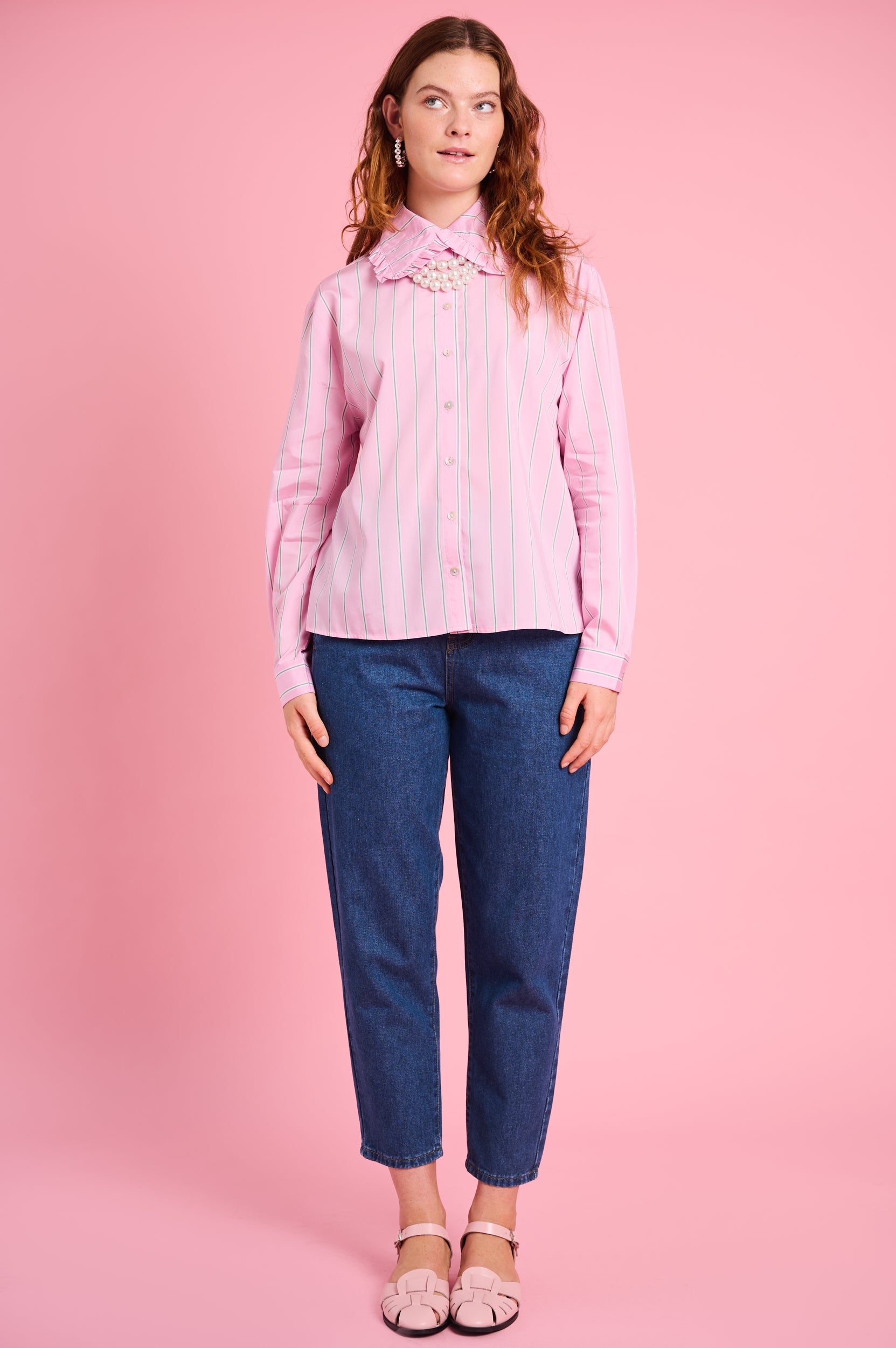 Model is wearing a pink stripe peter pan shirt with denim jeans