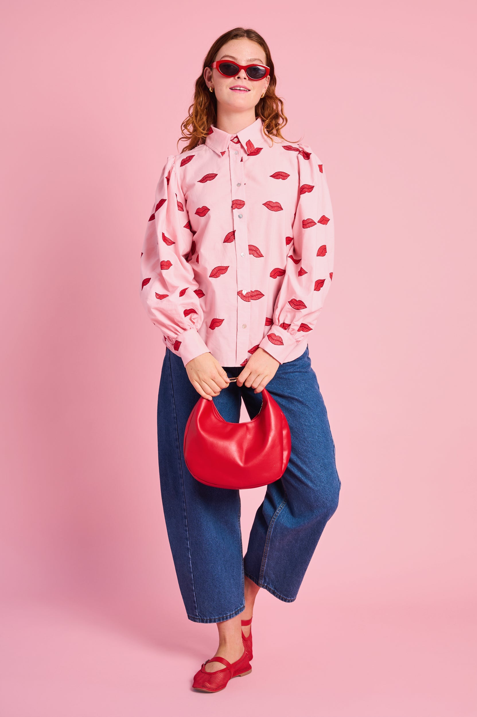 Model is wearing a embroidered pink top with denim jeans and red shoes