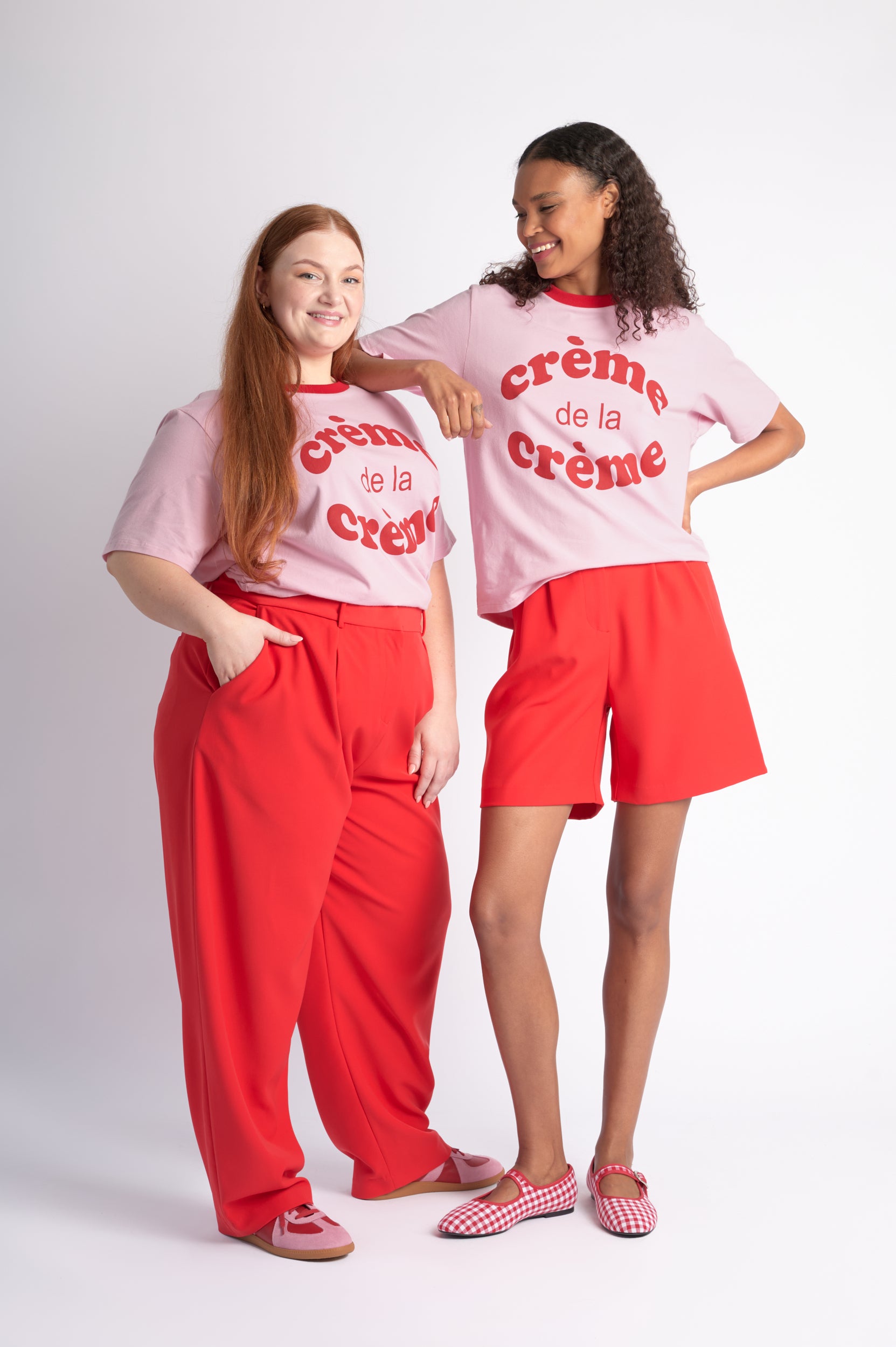 Two people wearing matching 'creme de la creme' shirts and red pants on a white background