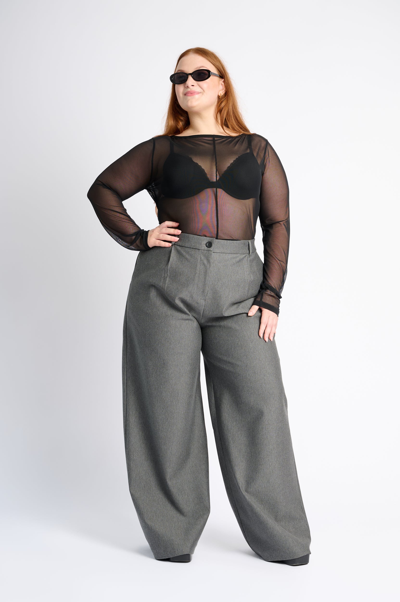 Person wearing a black sheer top and gray wide-leg pants on a white background