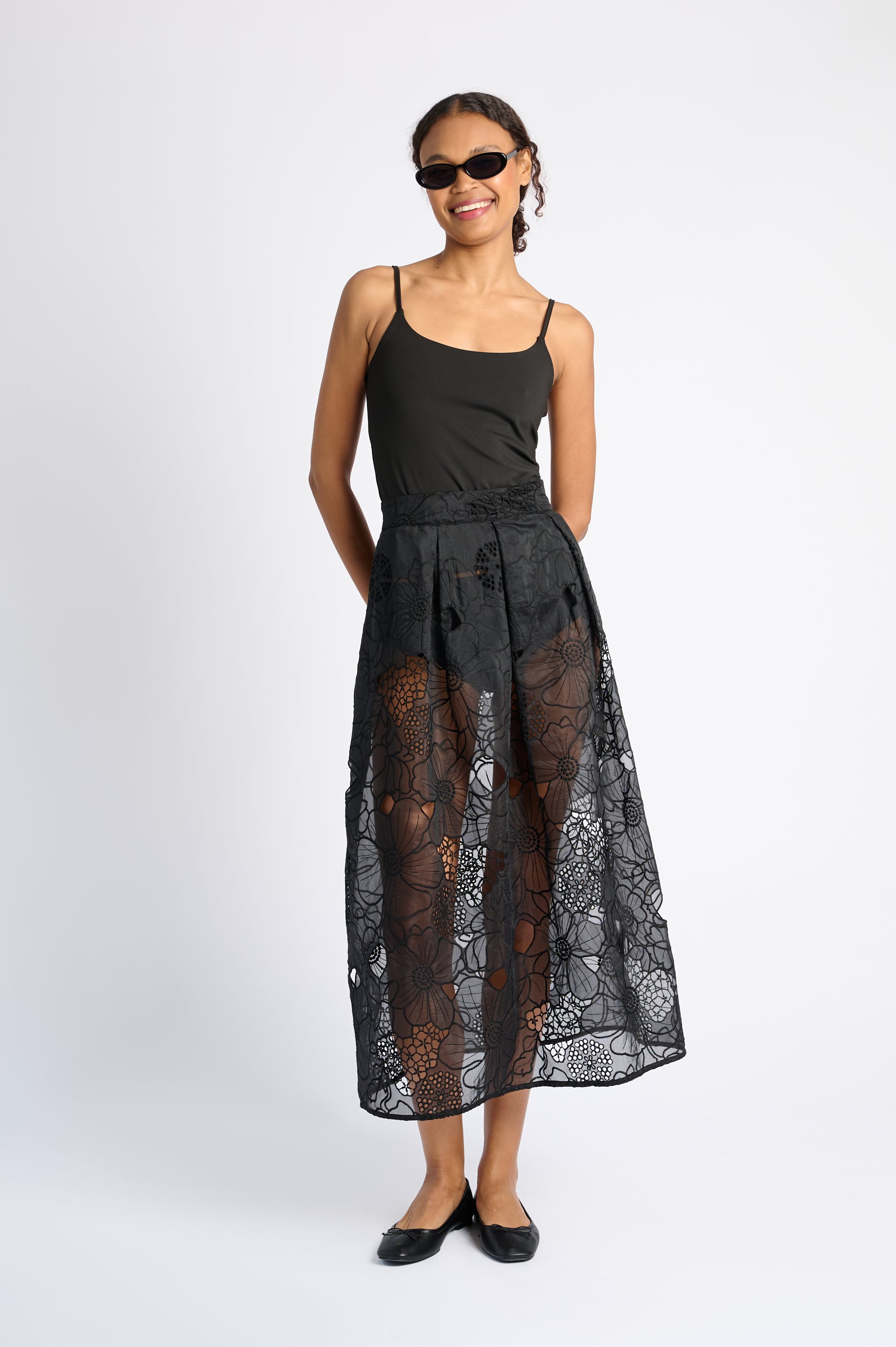 Woman wearing a black sleeveless top and sheer black lace skirt on a white background