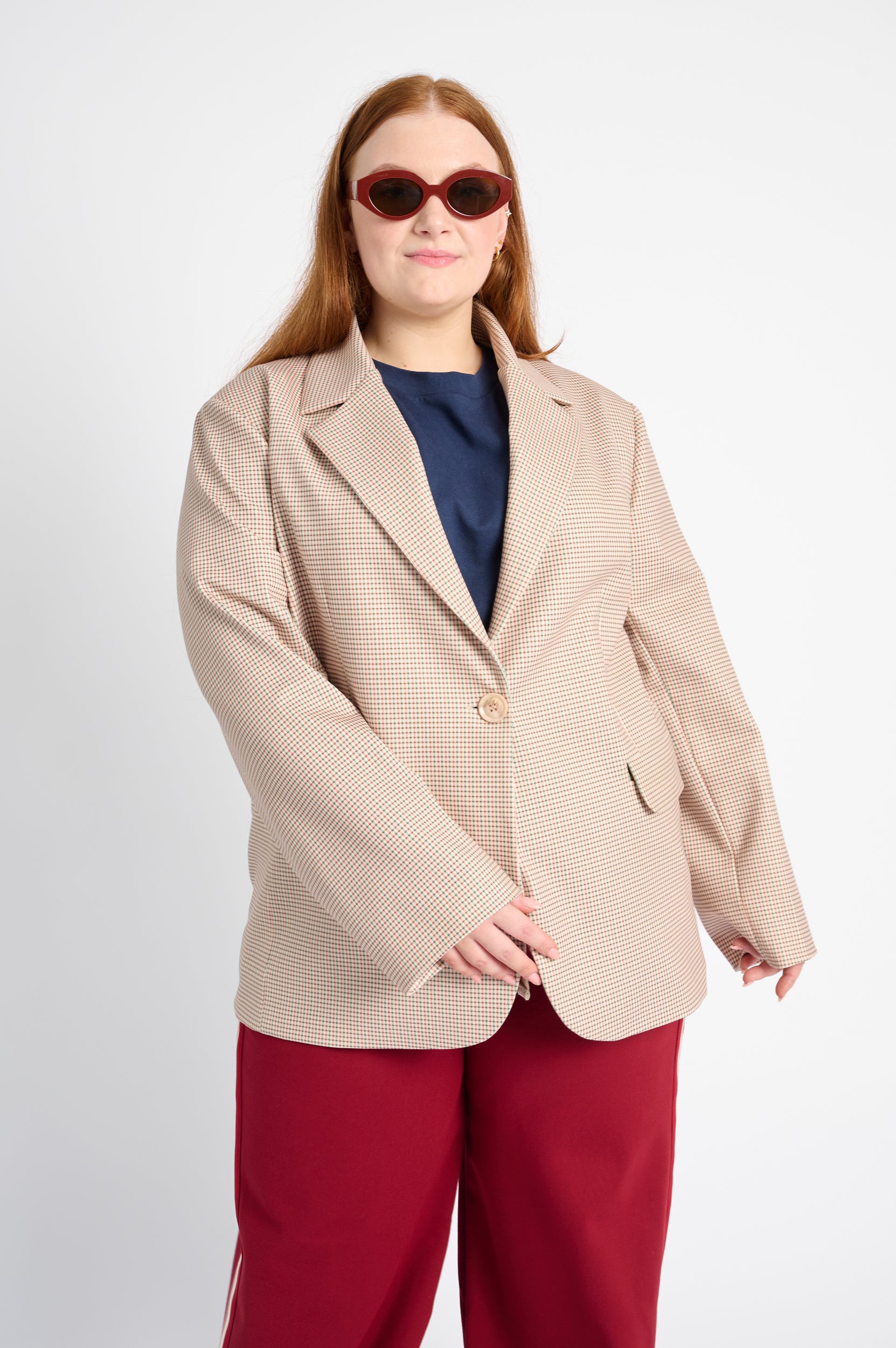 Model is wearing a beige tailored jacket with red pants and red sunglasses