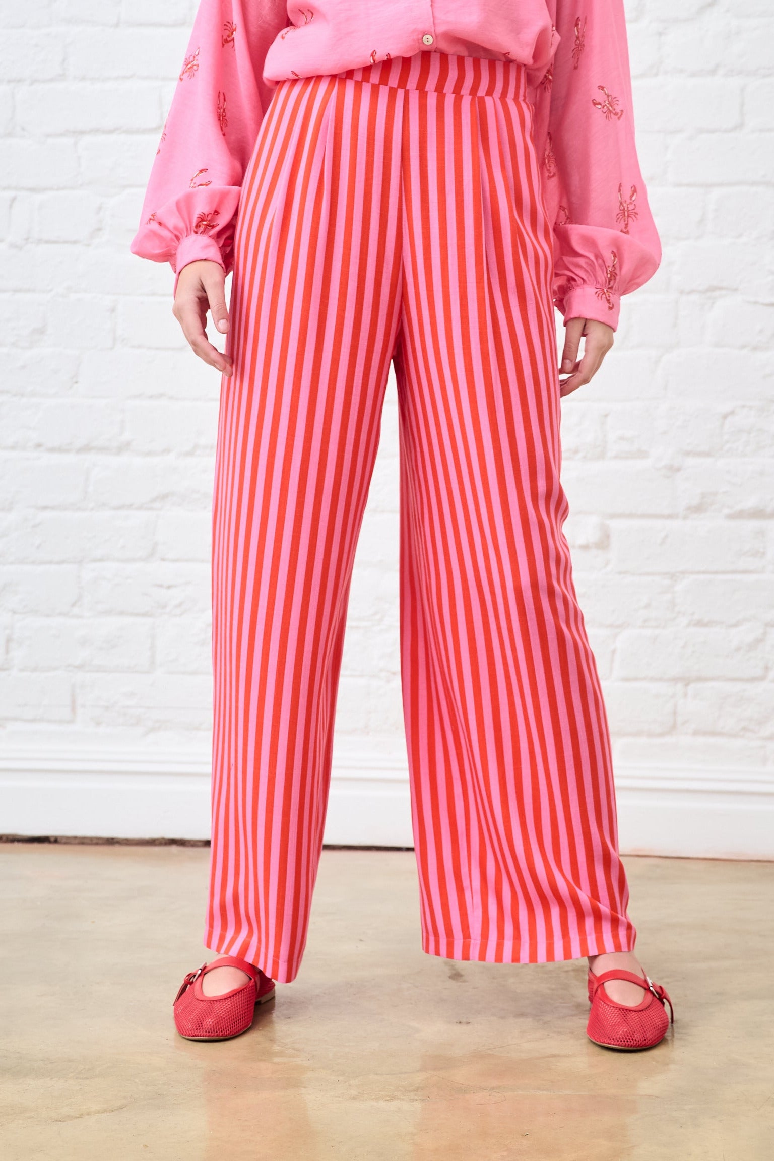 Person wearing pink striped pants and a pink top against a white brick wall.