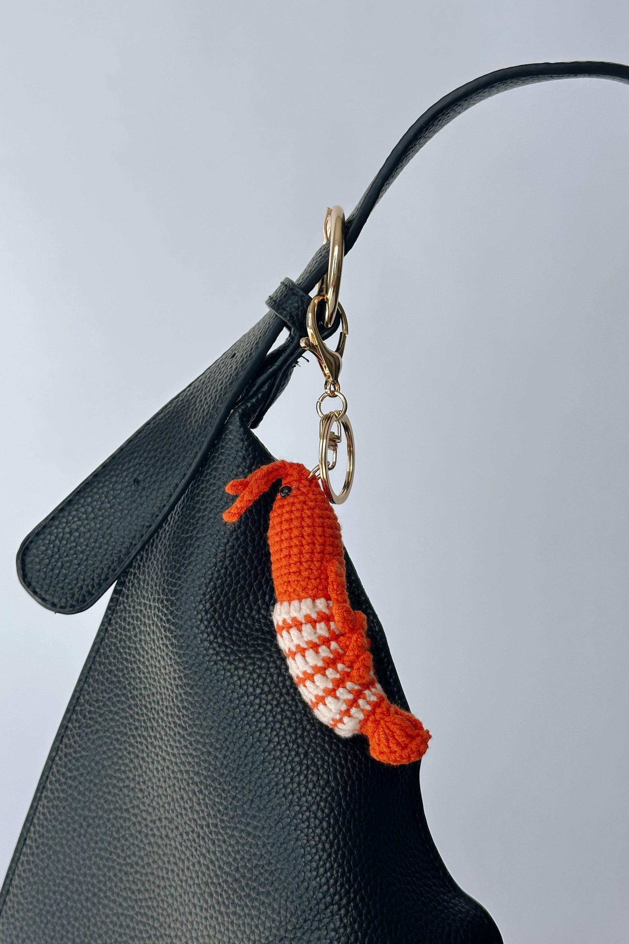 Crocheted keychain attached to a black handbag against a light gray background