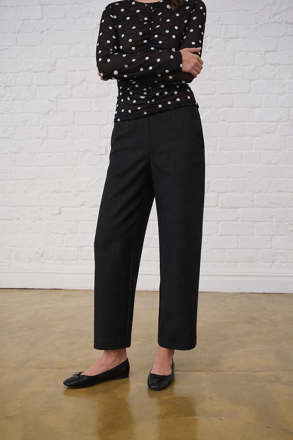 Model is wearing black barrel leg ponti pants with a polka dot sheer top and black pumps