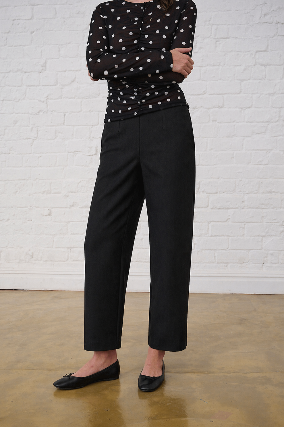 Model is wearing black barrel leg ponti pants with a polka dot sheer top and black pumps