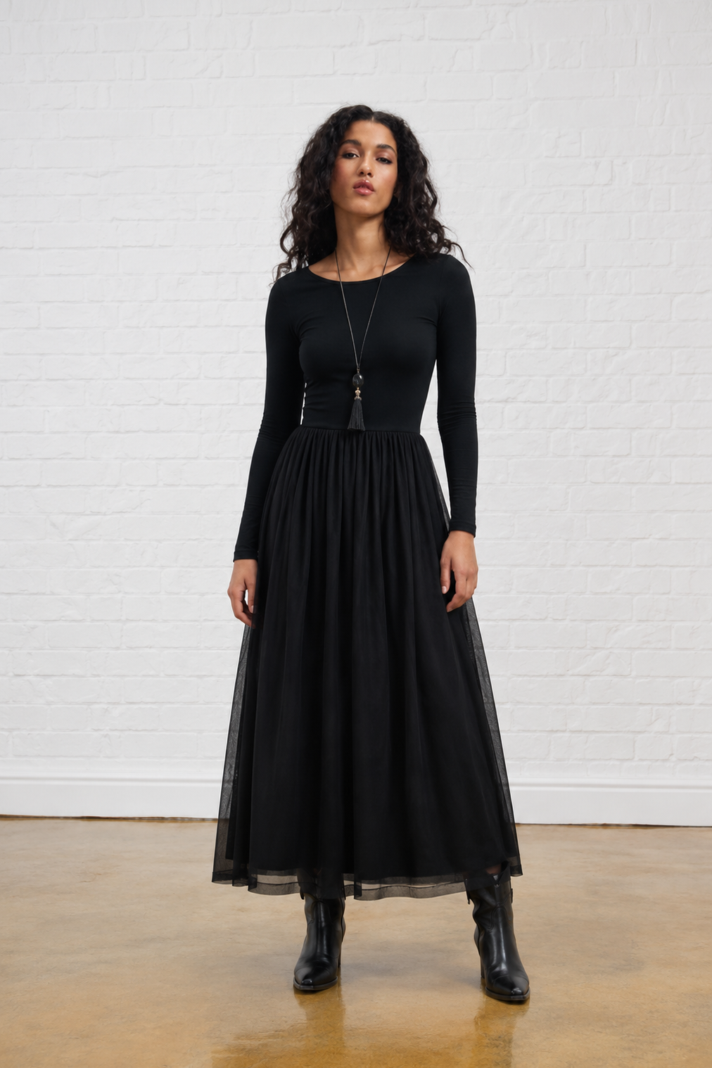 Model is wearing a black mesh combo dress with black boots and a tassel accessory 