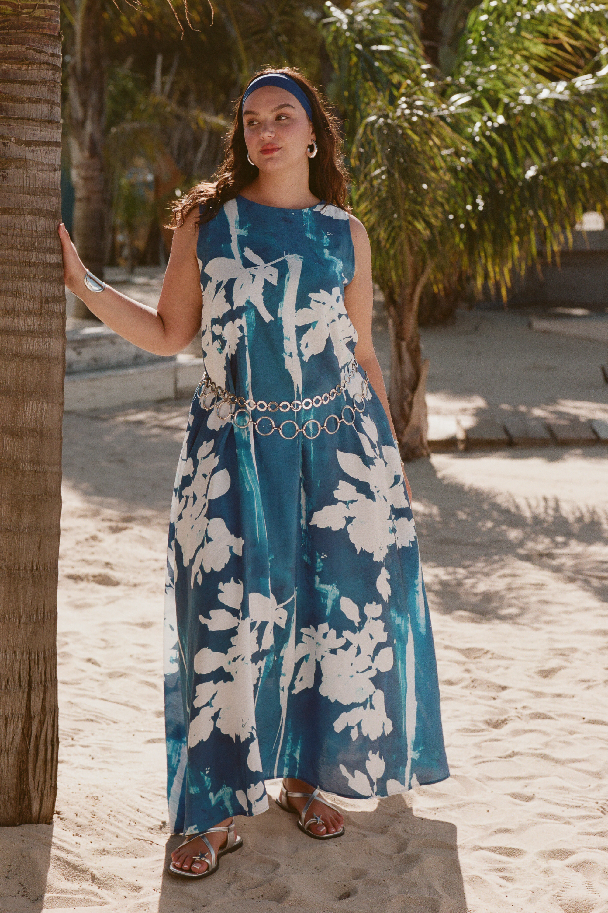 Woman in a blue floral dress standing next to a palm tree in a tropical setting