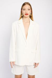 Model is wearing a white suit consisting of a tailored, lined blazer and pleated tailored shorts