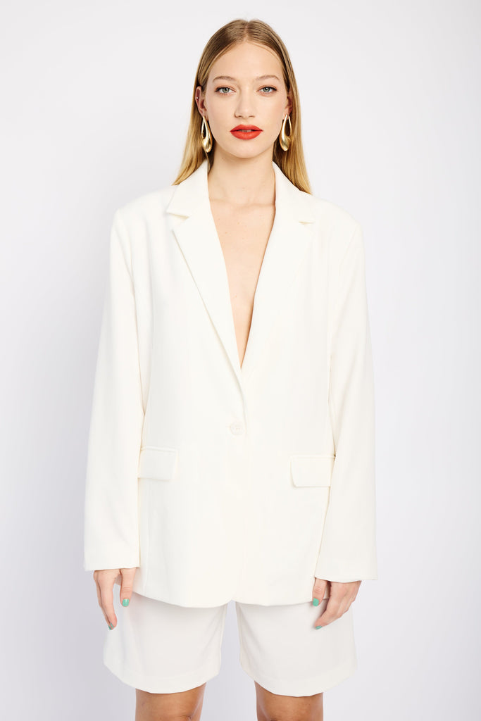 Model is wearing a white suit consisting of a tailored, lined blazer and pleated tailored shorts