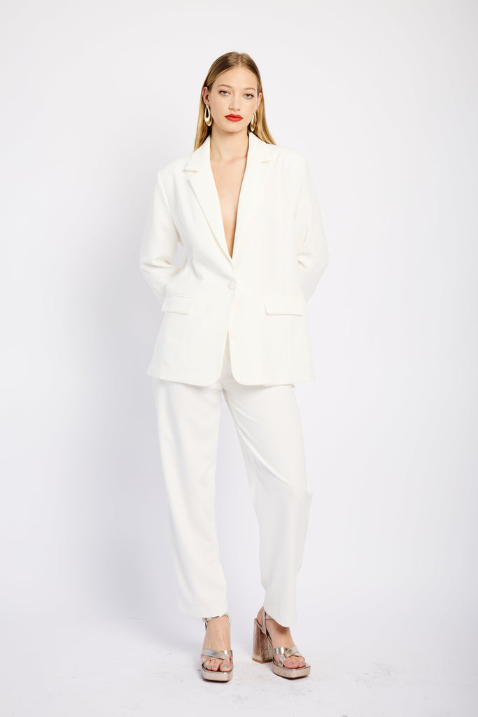 Model is wearing a white suit with a blazer and a pair of formal tapered leg pants 