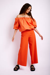 Model is wearing an orange off the shoulder bubble top with elbow length sleeves 