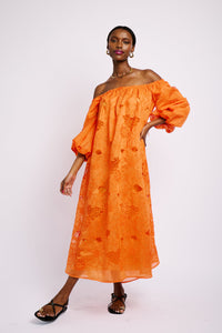 Model is wearing an off the shoulder midi length dress made of anglaise embroidered fabric. It has three quarter length sleeves and is lined.