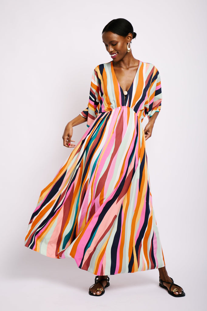 Model is wearing a colourful striped maxi dress, with a deep v-neckline, elasticated waist, flared sleeves and bead detail.