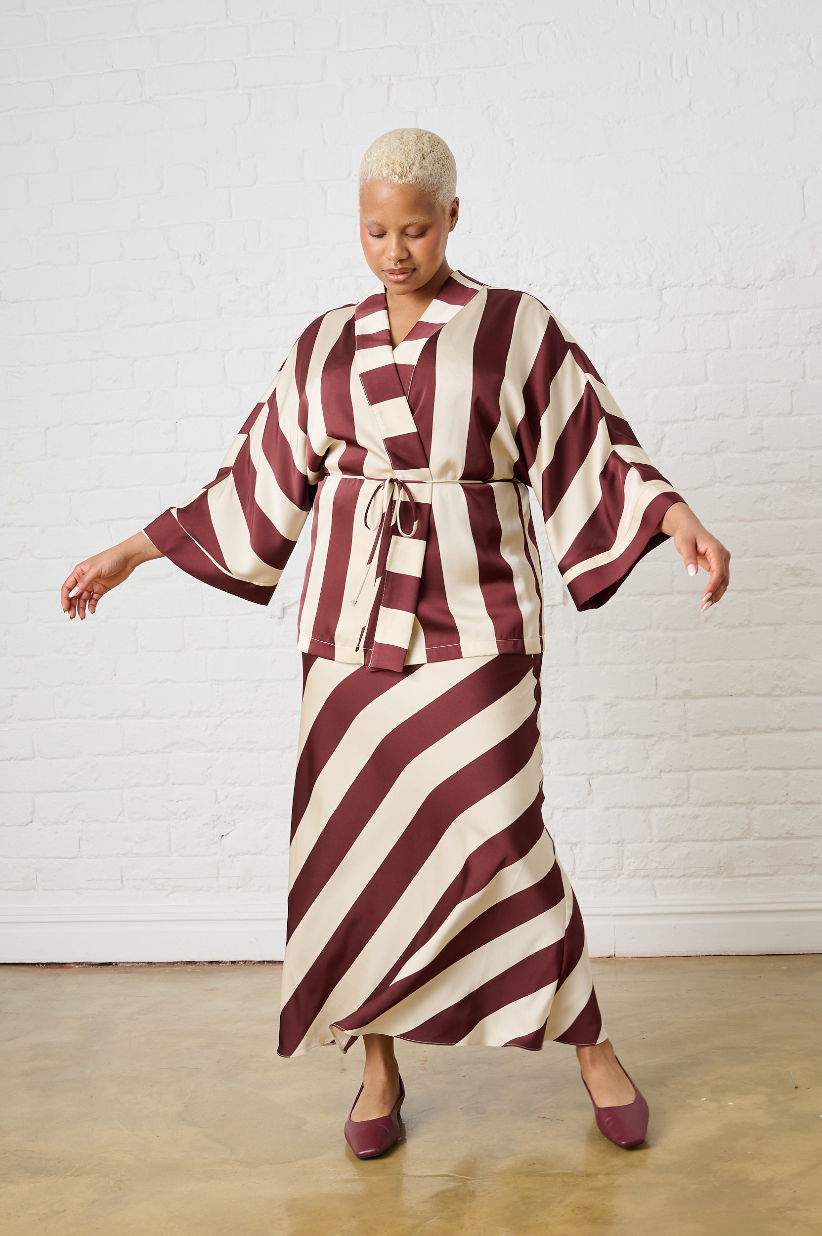 Woman wearing a maroon and white striped dress against a white brick wall.