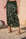 A model wearing a dark olive green sequined midi skirt and beige block-heel sandals, standing outdoors against a pink stucco wall.
