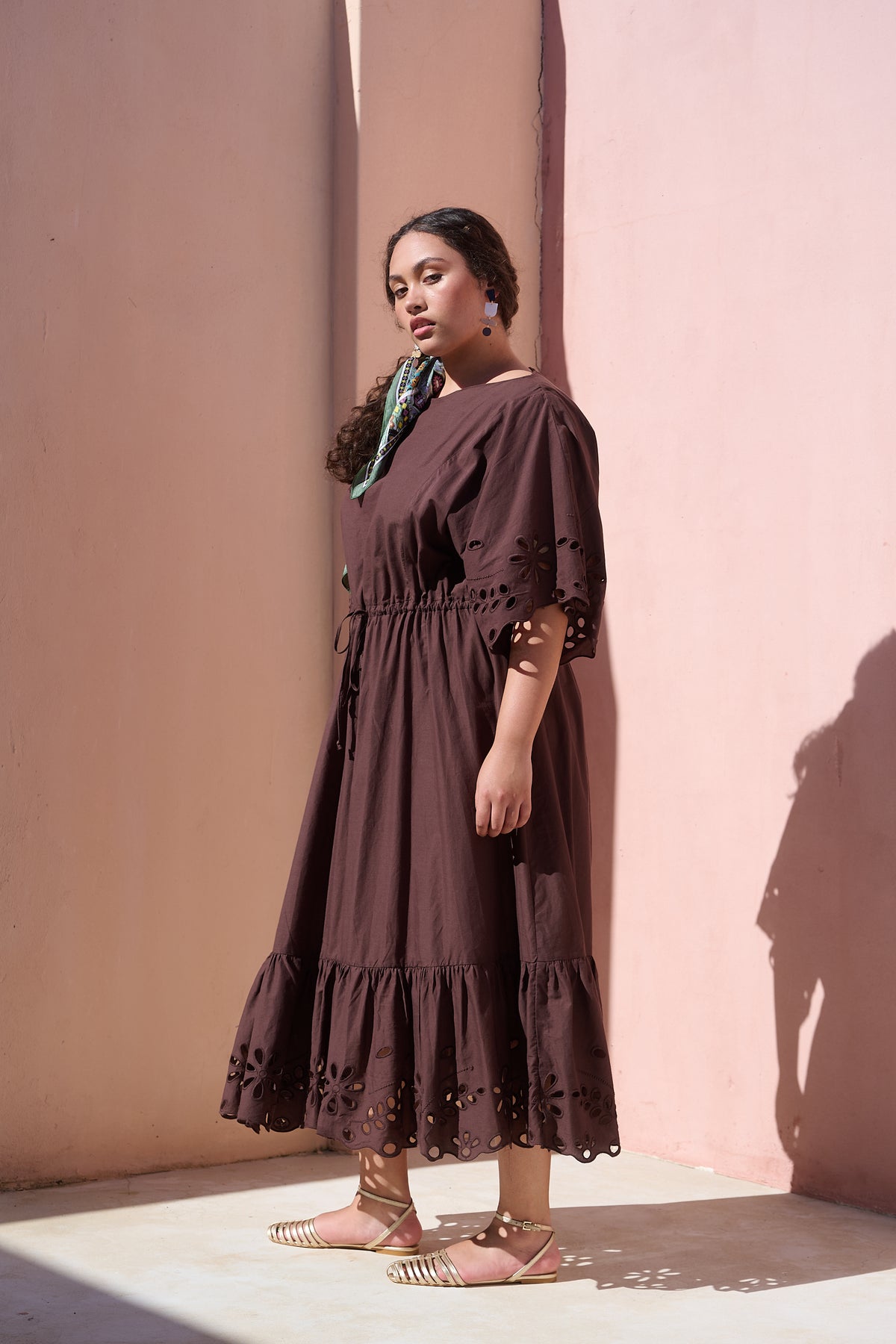 Model wearing chocolate cotton tiered dress with broderie anglaise
