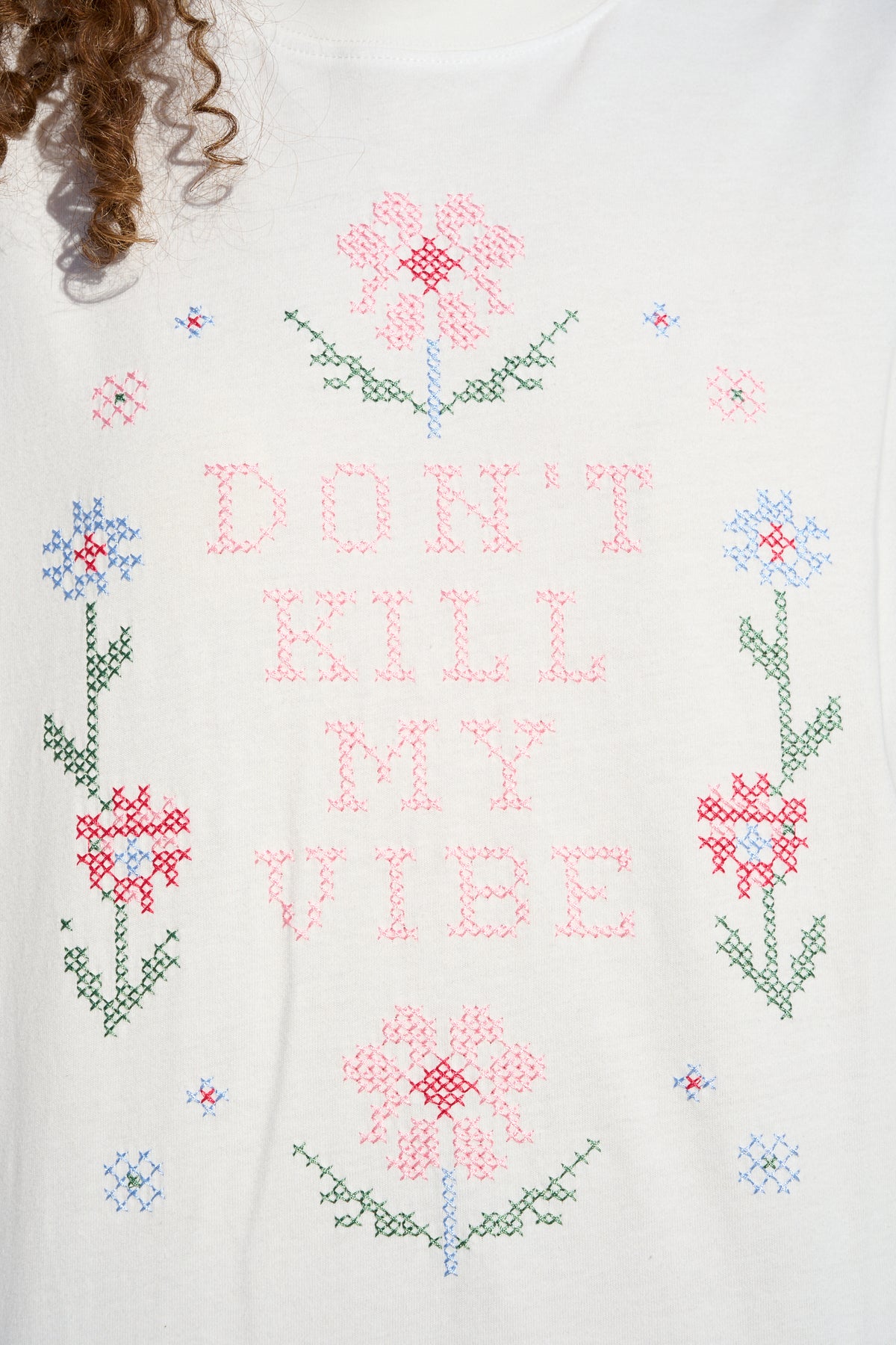 Model wearing white T-shirt with floral cross stitch detail