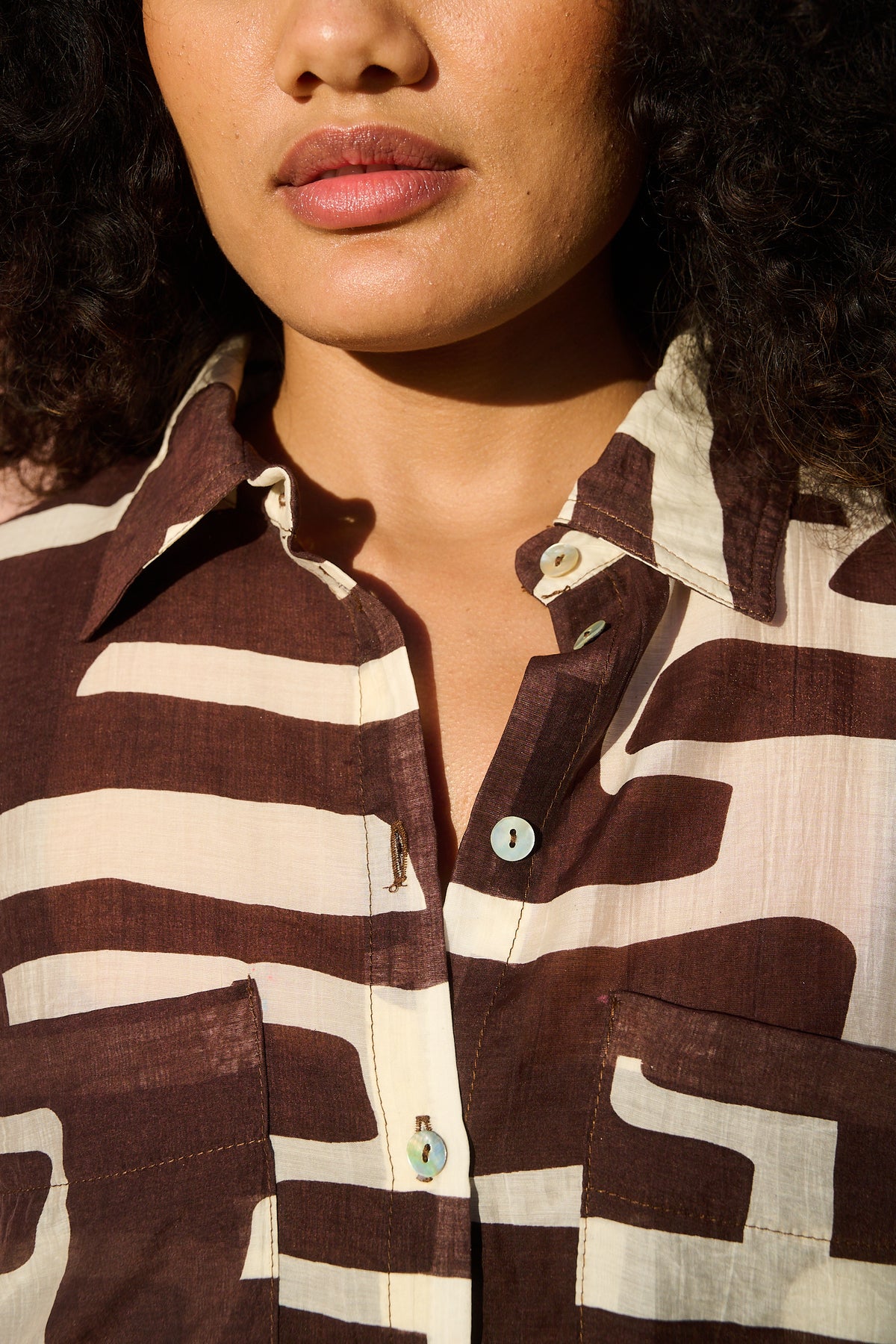 Close-up of a person wearing a brown and cream geometric button-up shirt, with mother of pearl buttons