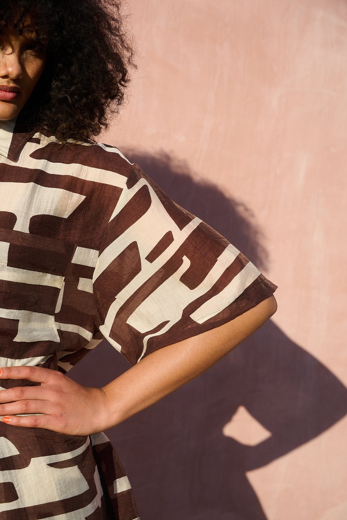 A close-up sleeve shot of a model wearing a brown and cream abstract patterned shirt