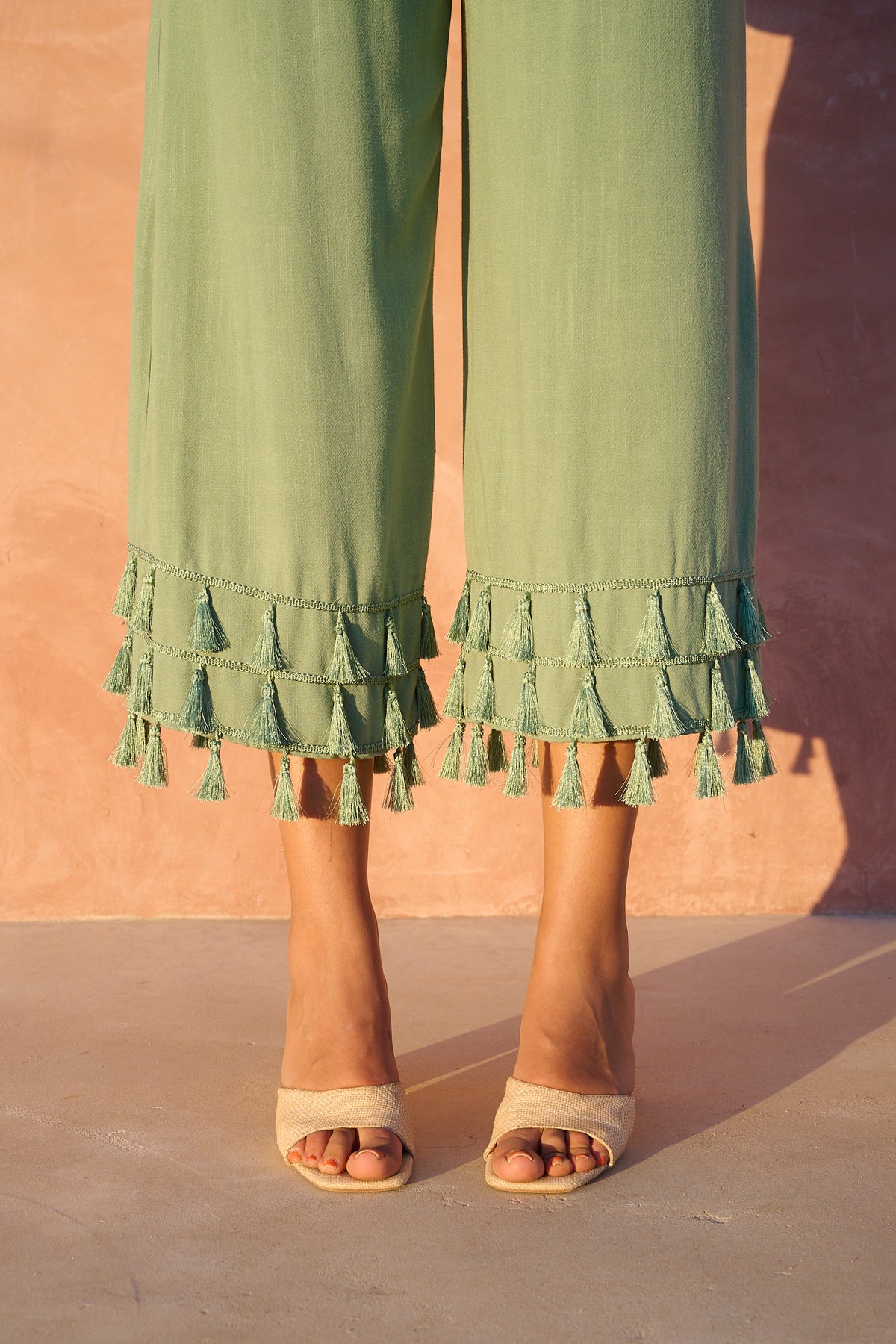 Model wearing shale green wide-leg cropped pants with tassel hems