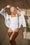 A happy model wearing a white bodysuit layered with a white shirt.
