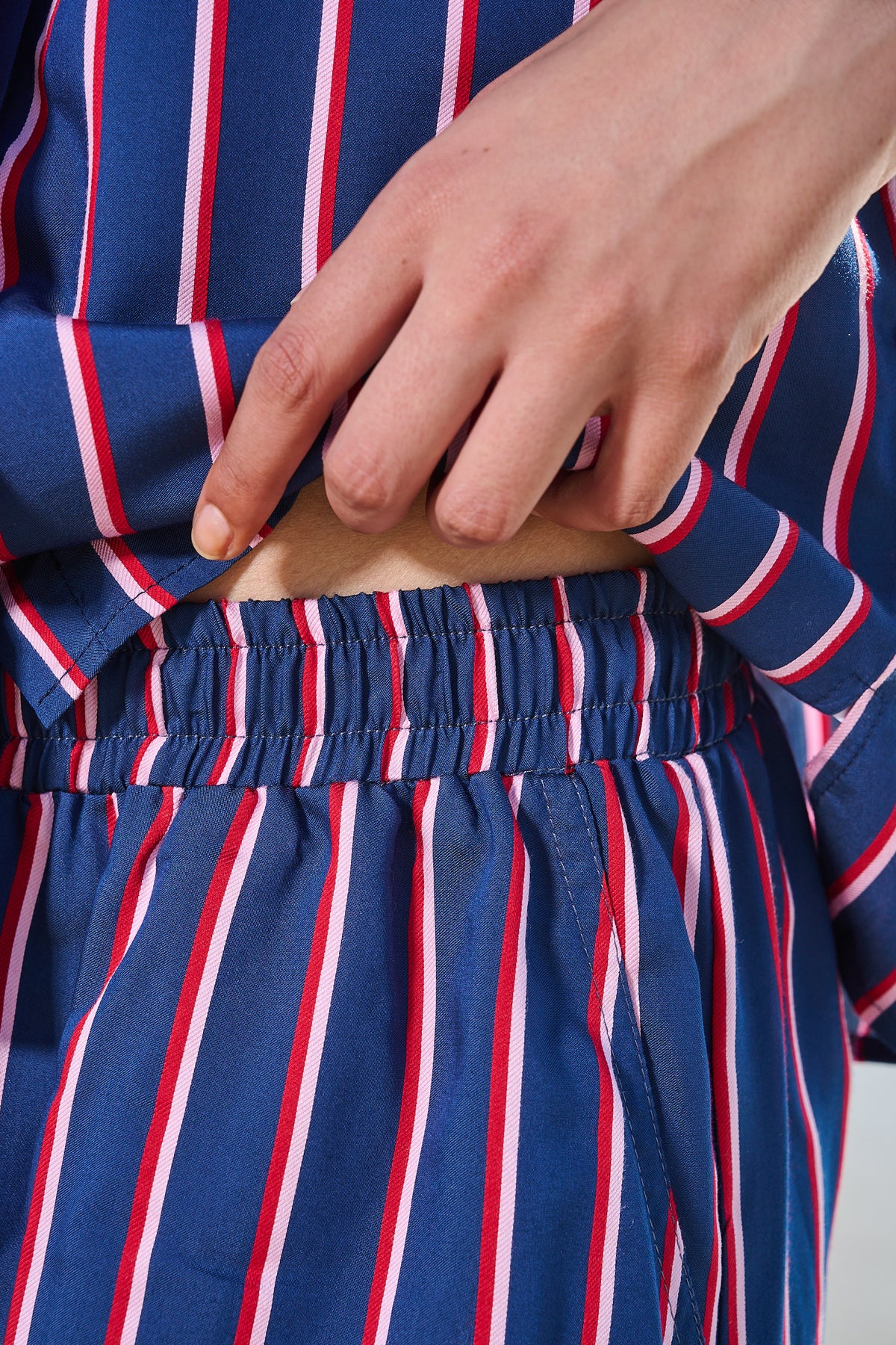 Close-up of a person wearing a blue striped garment with red and white vertical stripes, showing a hand pulling up the elastic waist area.