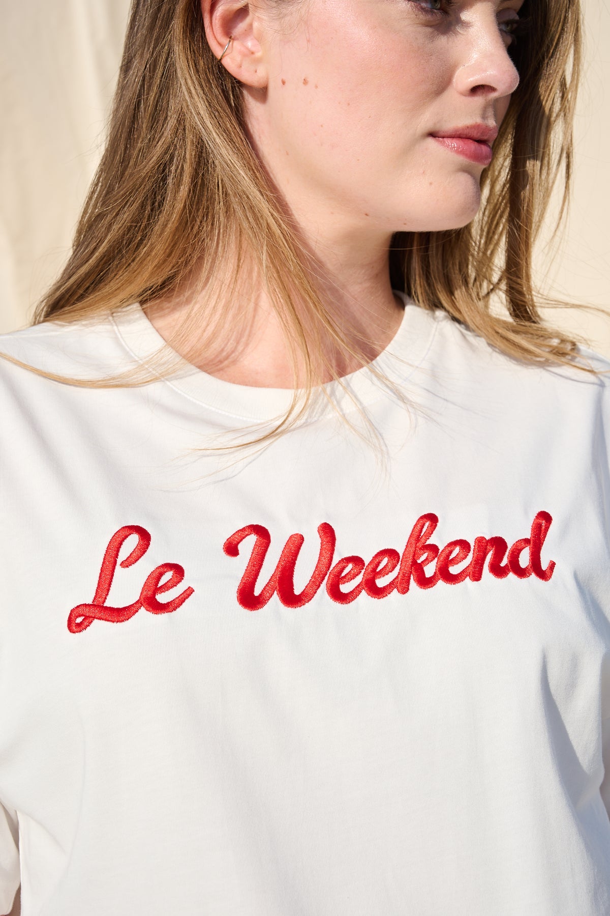 A close-up of a woman wearing a white crewneck T-shirt with 'Le Weekend' embroidered in red across the chest.