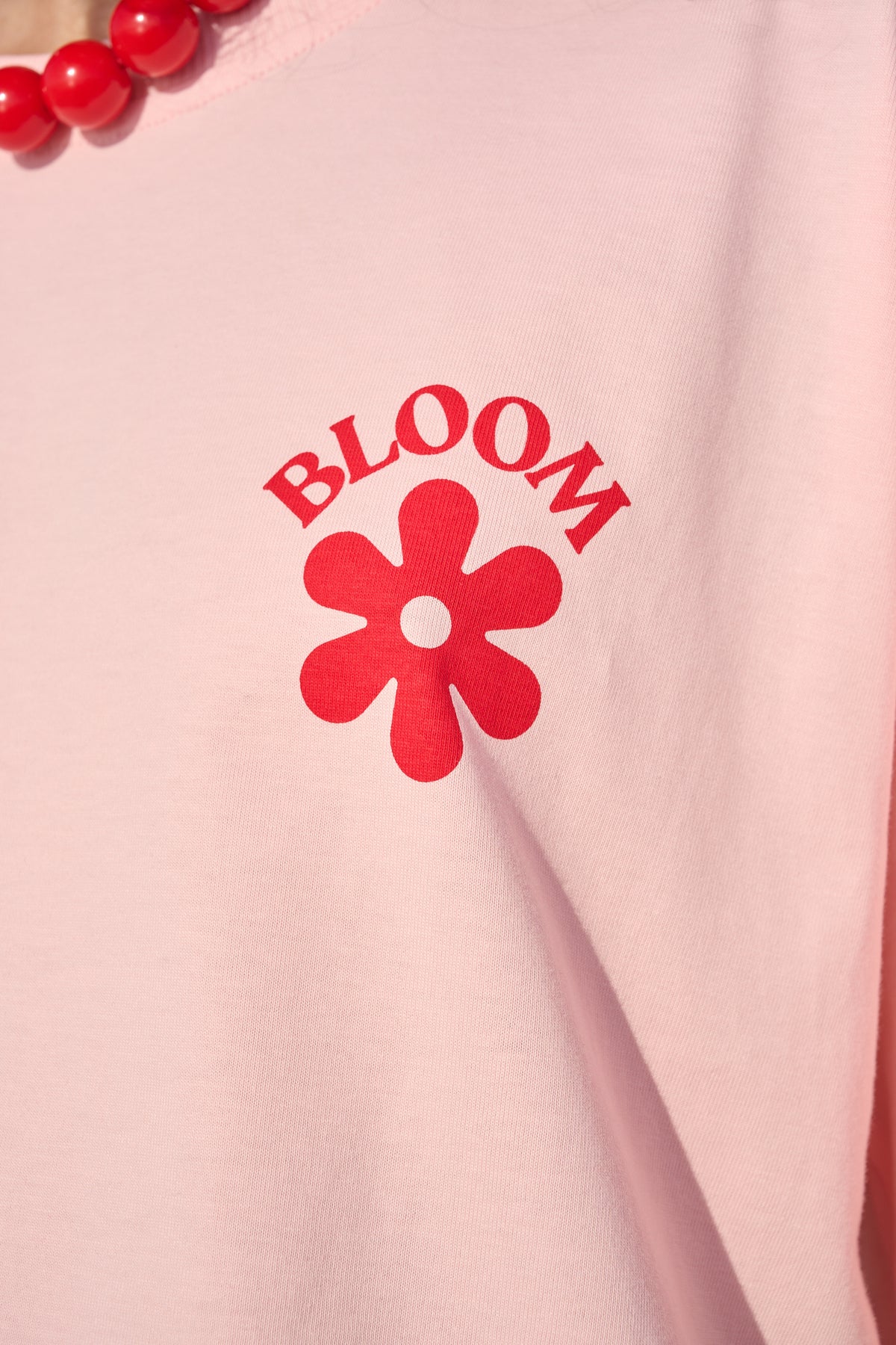 A close-up of a light pink sweatshirt featuring a red graphic print of a flower and the word 'BLOOM' on the chest.