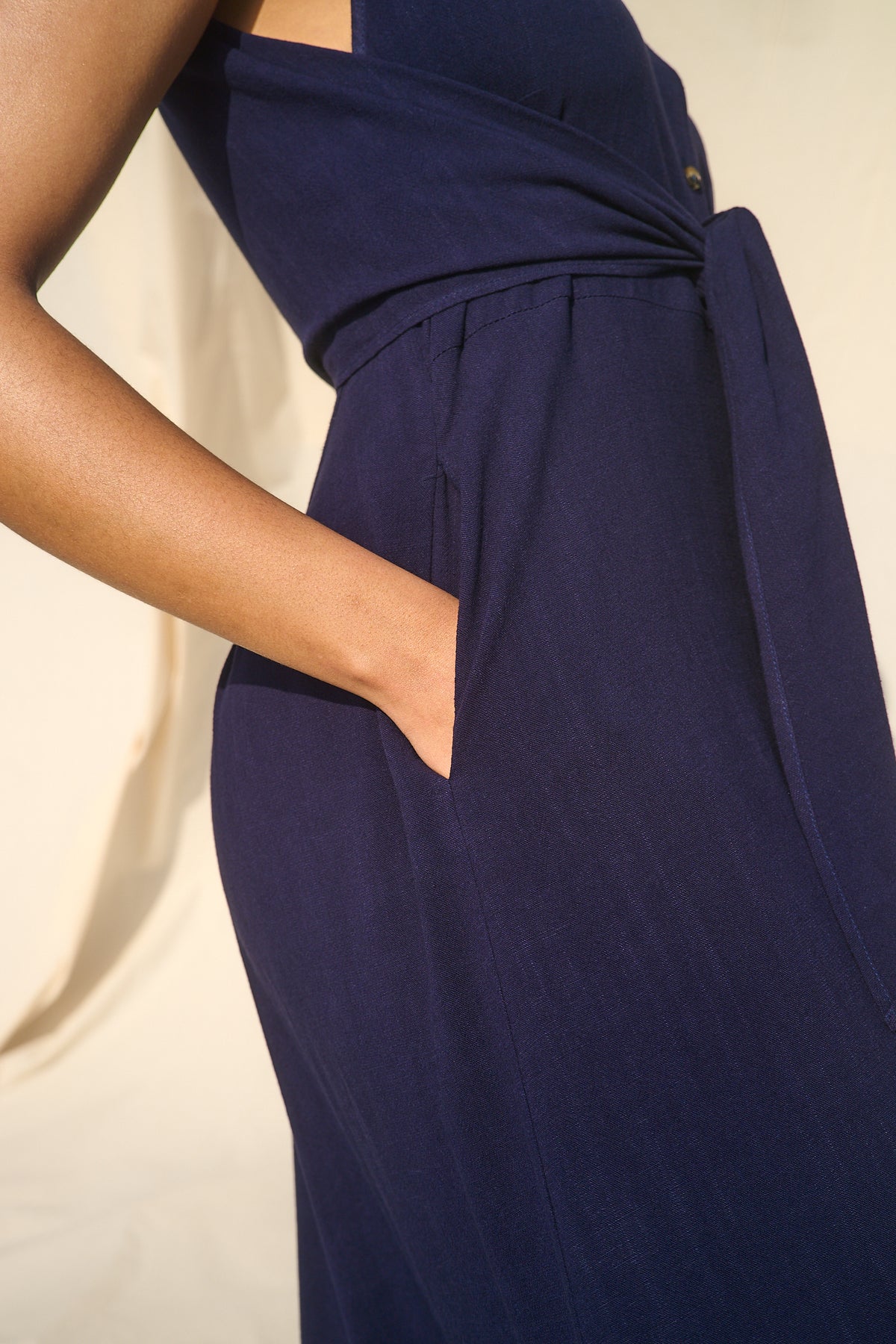 Close-up of a navy blue wrap-style dress with side pockets, shown on a model against a warm cream background.