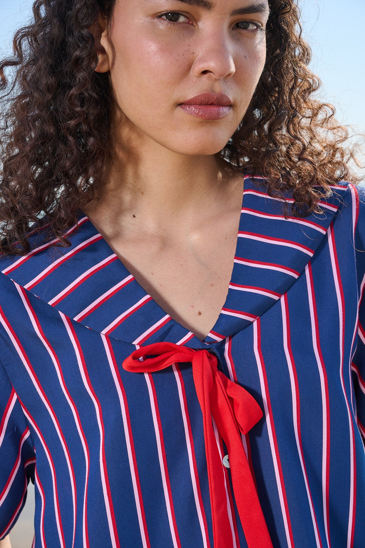 Close up of a sailor shirt with navy, red and pink stripes featuring a red tie t the front
