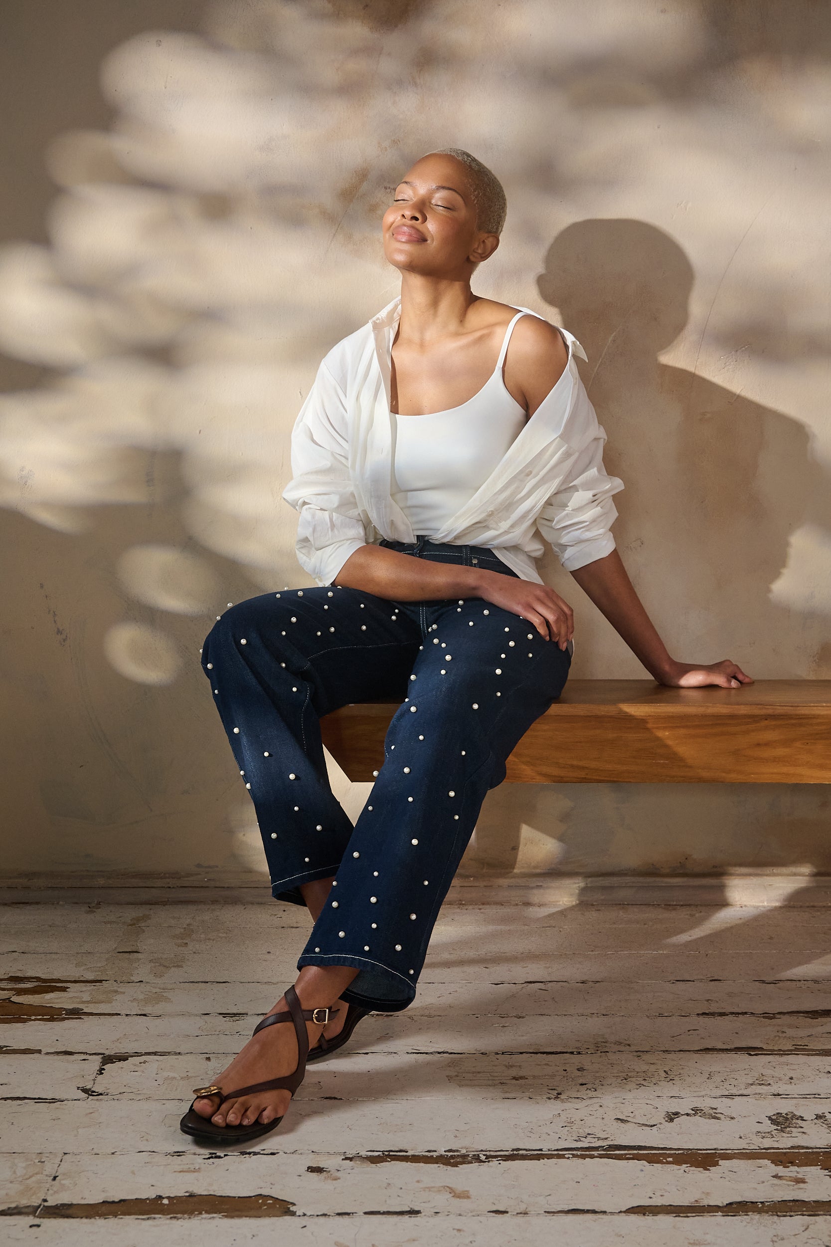Model is wearing dark wash straight jeans with pearl details and a white shirt