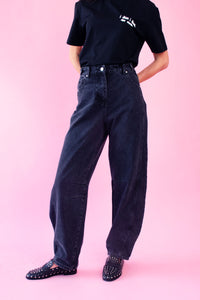 Model is wearing black barrel jeans with a black T-Shirt and black studded flat shoes