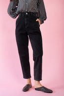 Model is wearing black denim mom jeans with a black and white blouse and black studded slip on shoes 