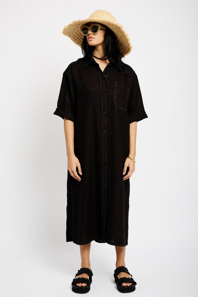 Model is wearing a black Linen Shirt Dress with short sleeves, a pocket and white contrast stitching 