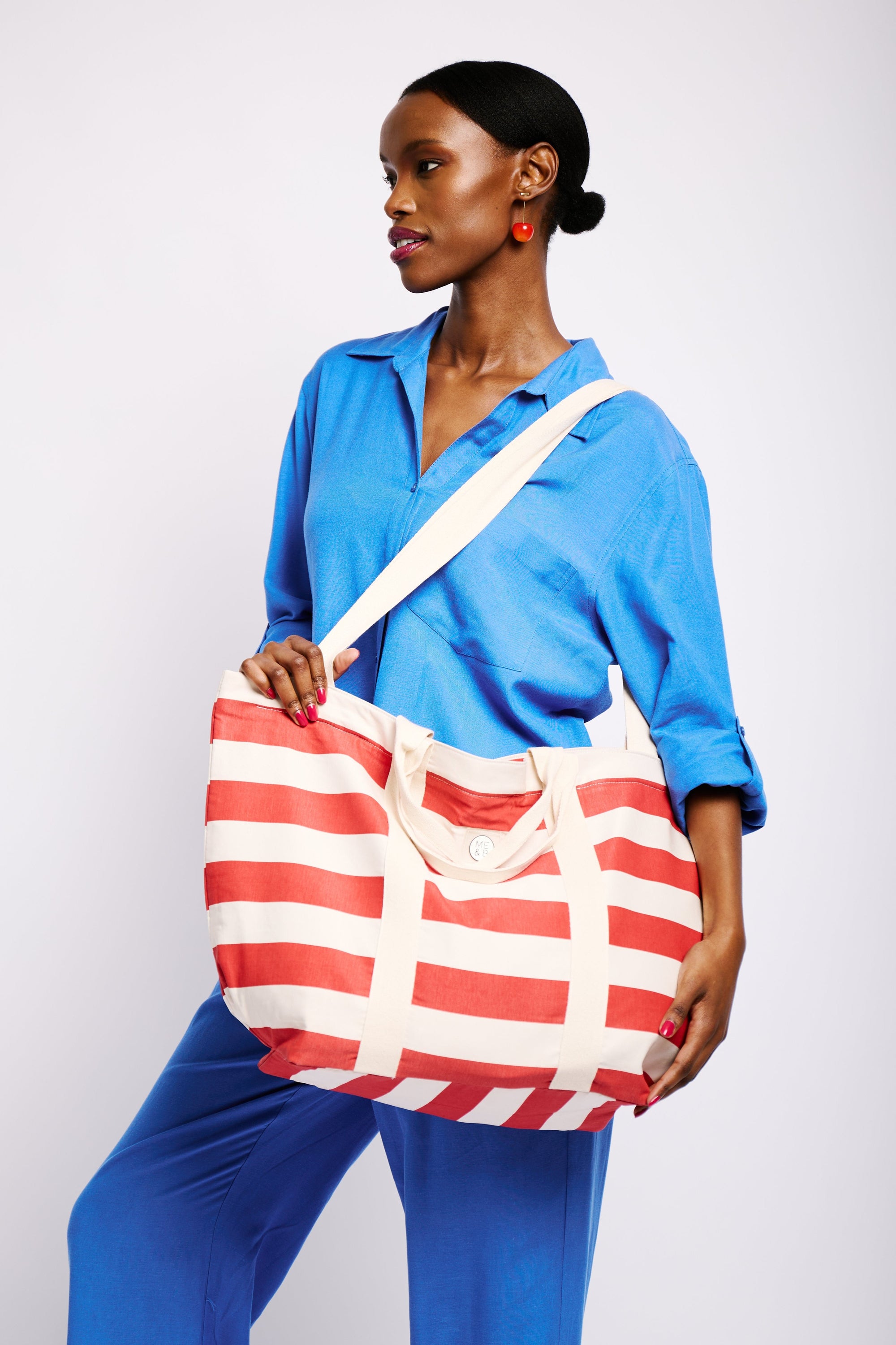 Model is wearing a red and white striped beach tote bag with shoulder and hand straps.