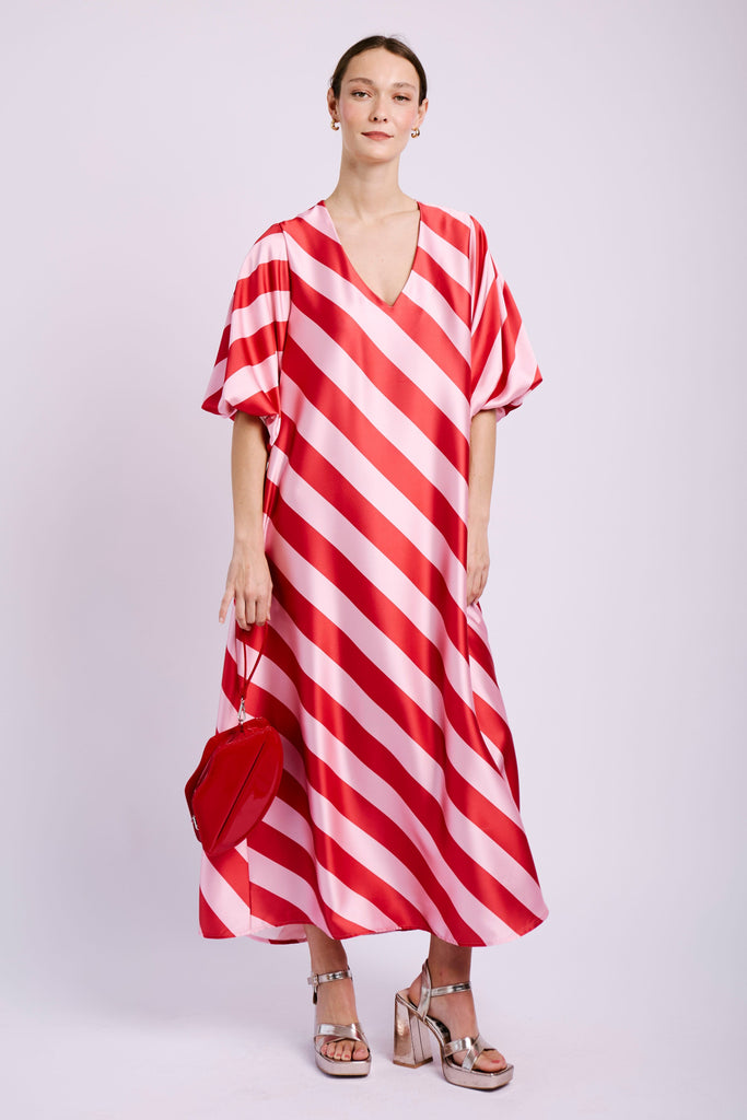 Model wearing pink and red striped dress with heels and lip handbag.