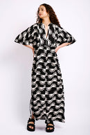 Model wearing black and white dress with sun print, black sandals and gold earrings